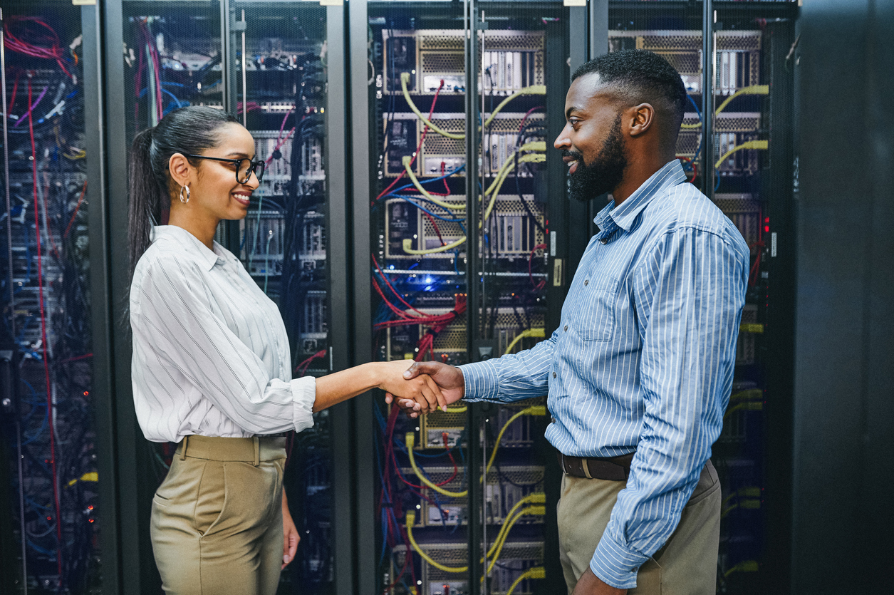 Shot of two young technicians shaking hands in a server room